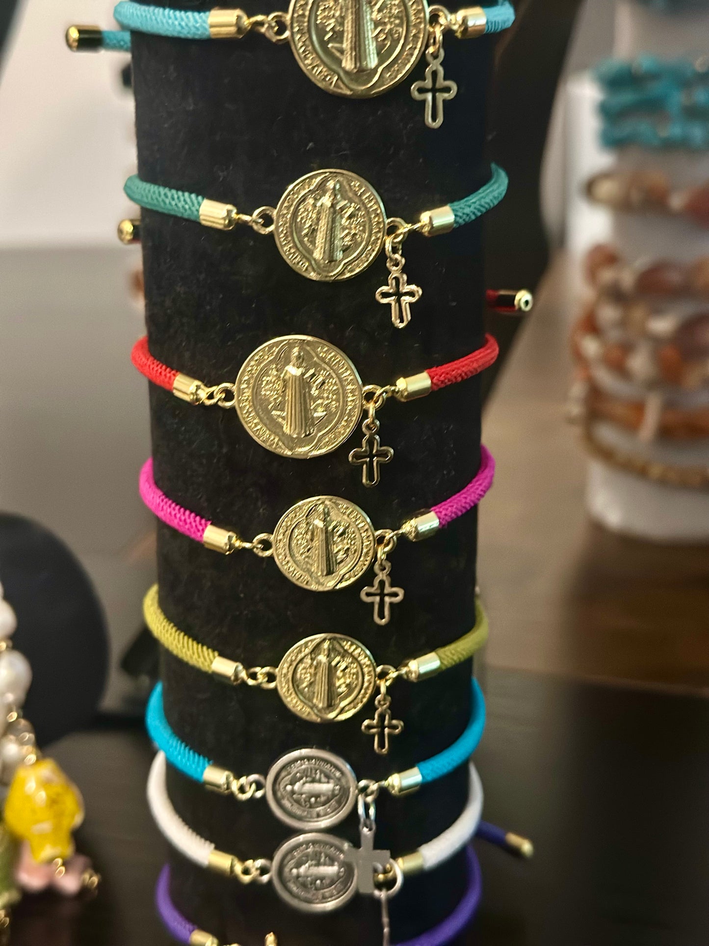 A- Pulseras de cordón con dijes de San Benito y Cruz
